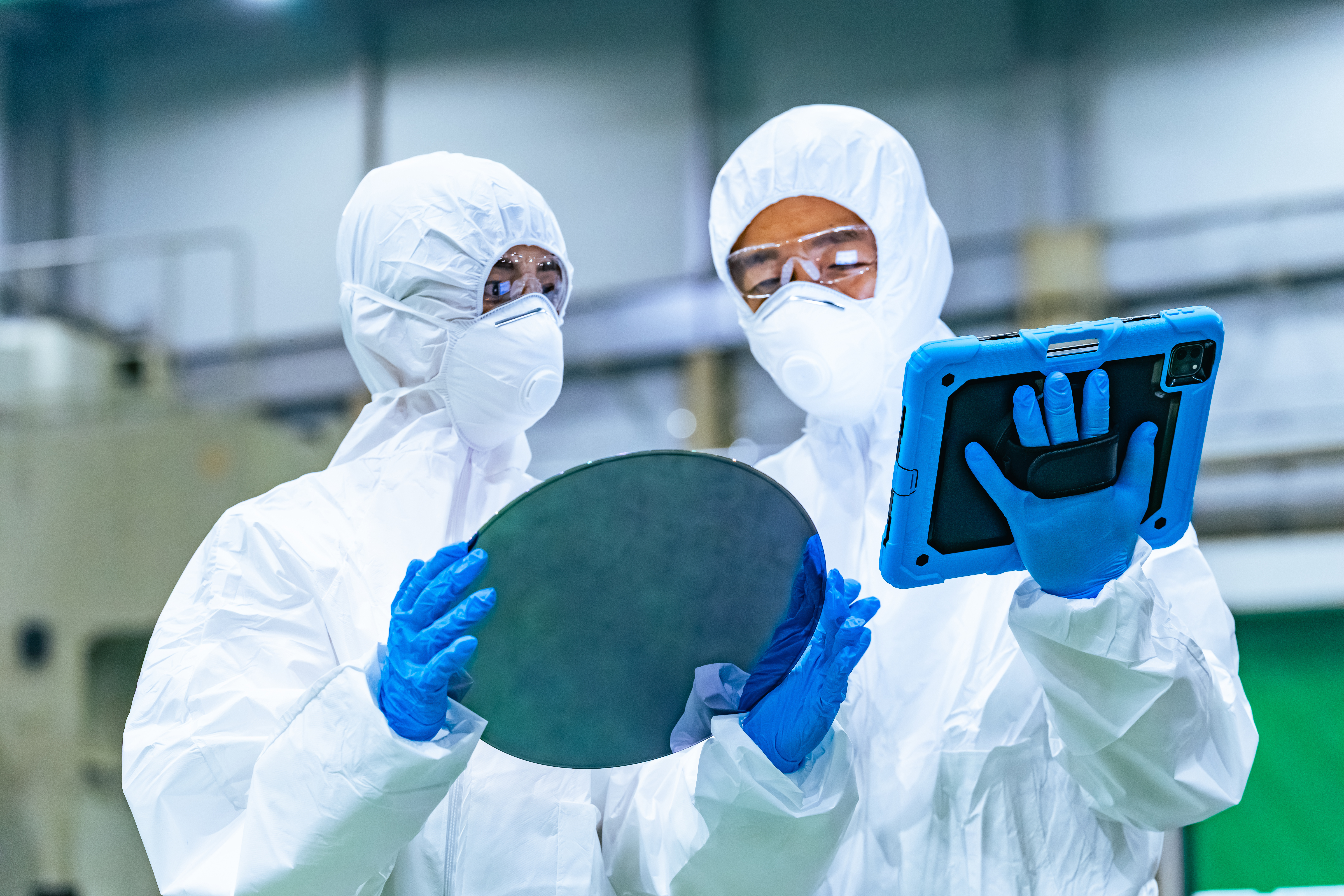 Mannelijke en vrouwelijke werknemers in beschermende kleding die in een halfgeleiderfabriek siliciumwafers inspecteren met behulp van tablets